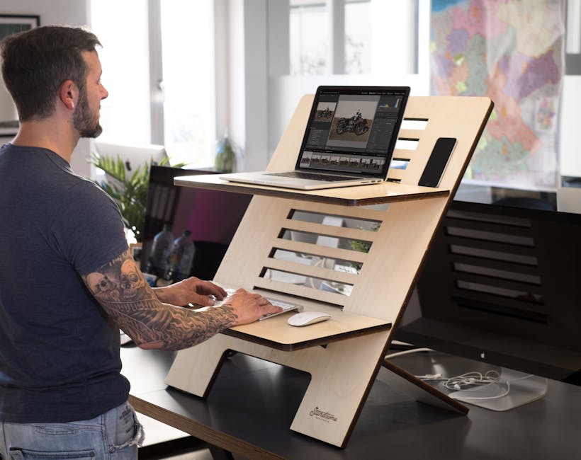 Man using a laptop on a modern standing desk in a bright office setting.